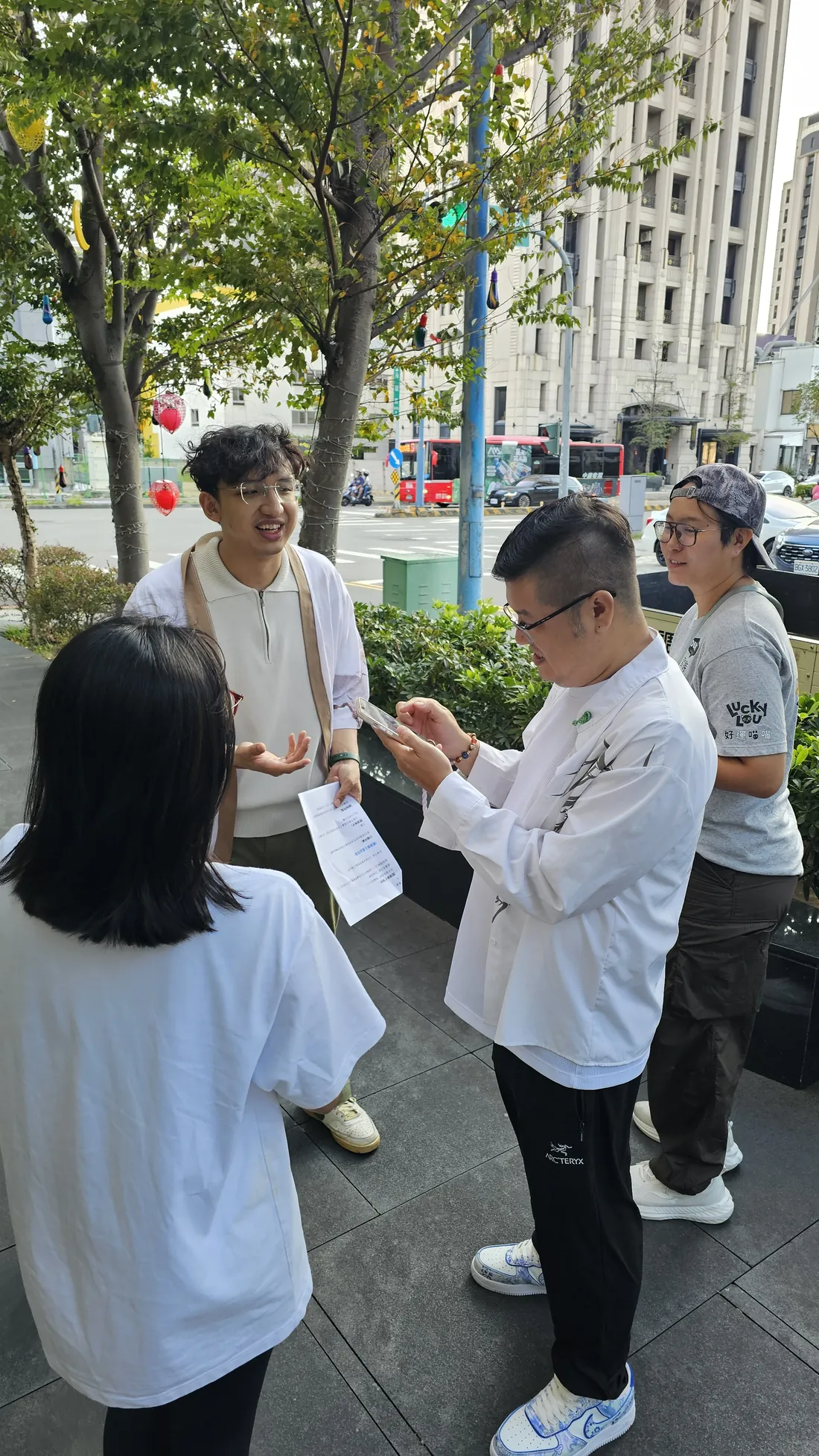 戶外街邊，蟬師拿著紙本一邊講解，三位學員圍著聽，其中一位拿手機對照